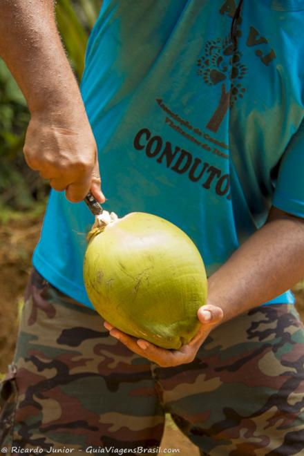 Imagem de um homem abrindo um coco enorme na Cachoeira do Tijuípe.